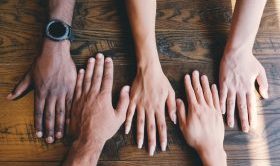 five hands on a dark brown tabletop
